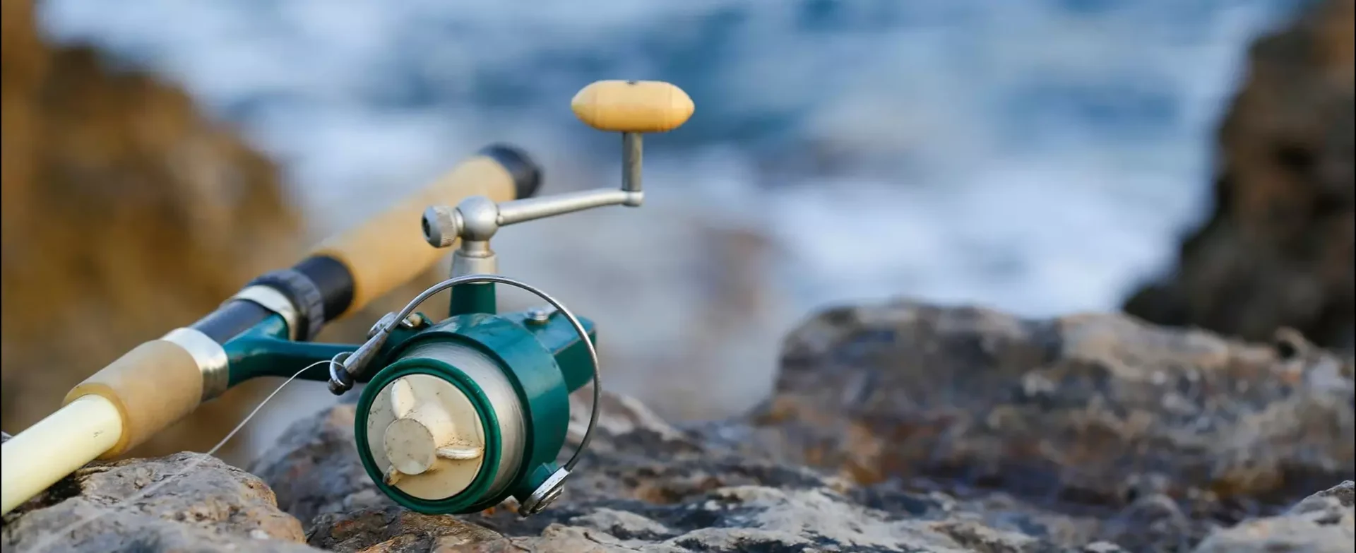 A fishing rod and reel on the rocks near water.